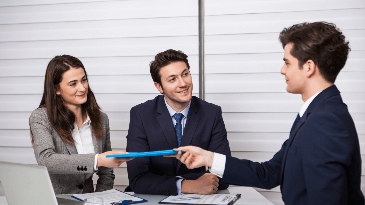An office team of 3 at a meeting. One team member passes a folder to another | Scott Legal, P.C. An office team of 3 at a meeting. One team member passes a folder to another