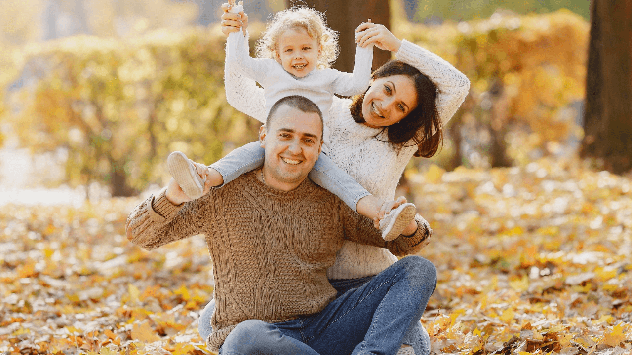 A family of 3 sitting in a pile of leaves while smiling | Scott Legal, P.C. A family of 3 sitting in a pile of leaves while smiling