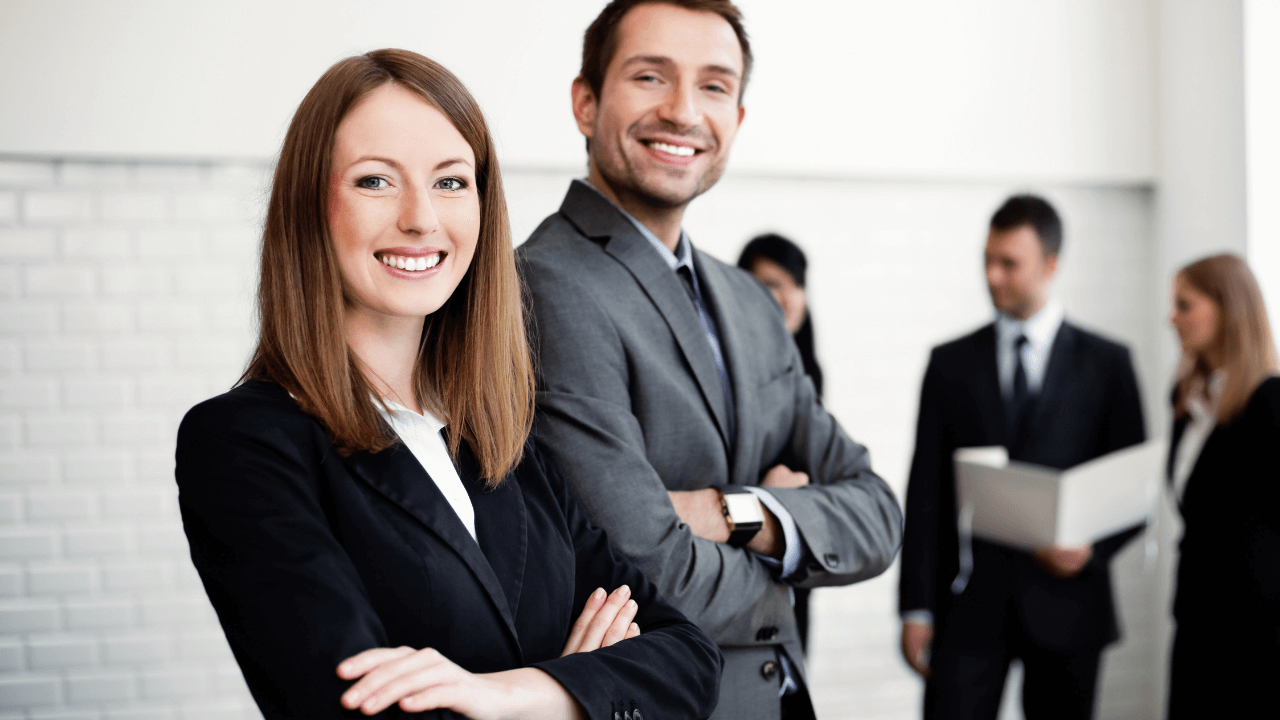 Two business people smiling in an office full of people | Scott Legal, P.C. Two business people smiling in an office full of people