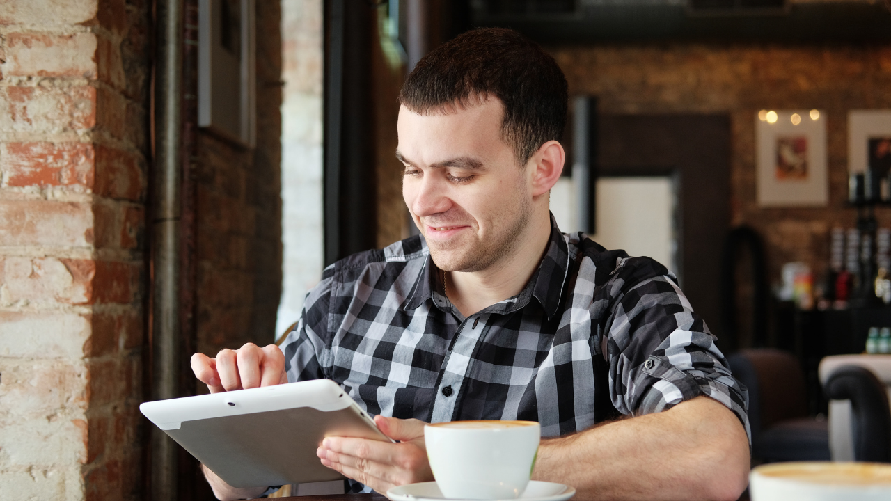 A man sitting in a cafe on his tablet | Scott Legal, P.C. A man sitting in a cafe on his tablet