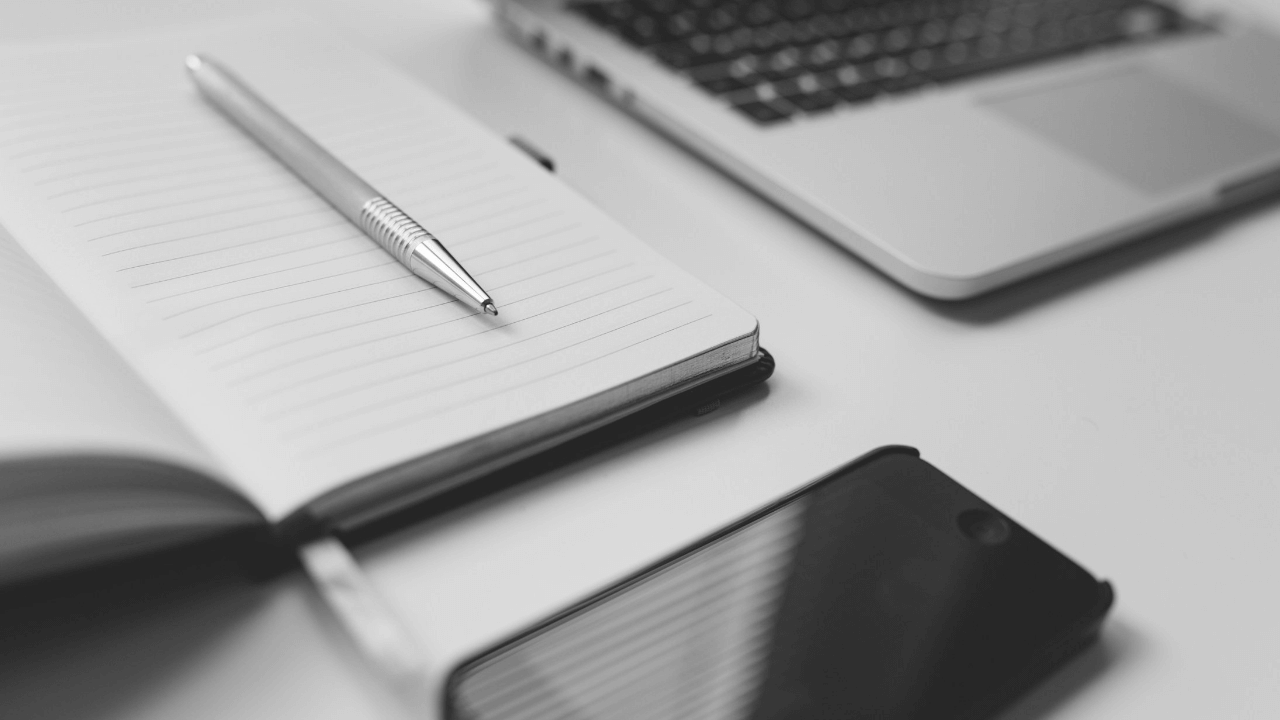 a pen, notebook, phone and laptop on a desk