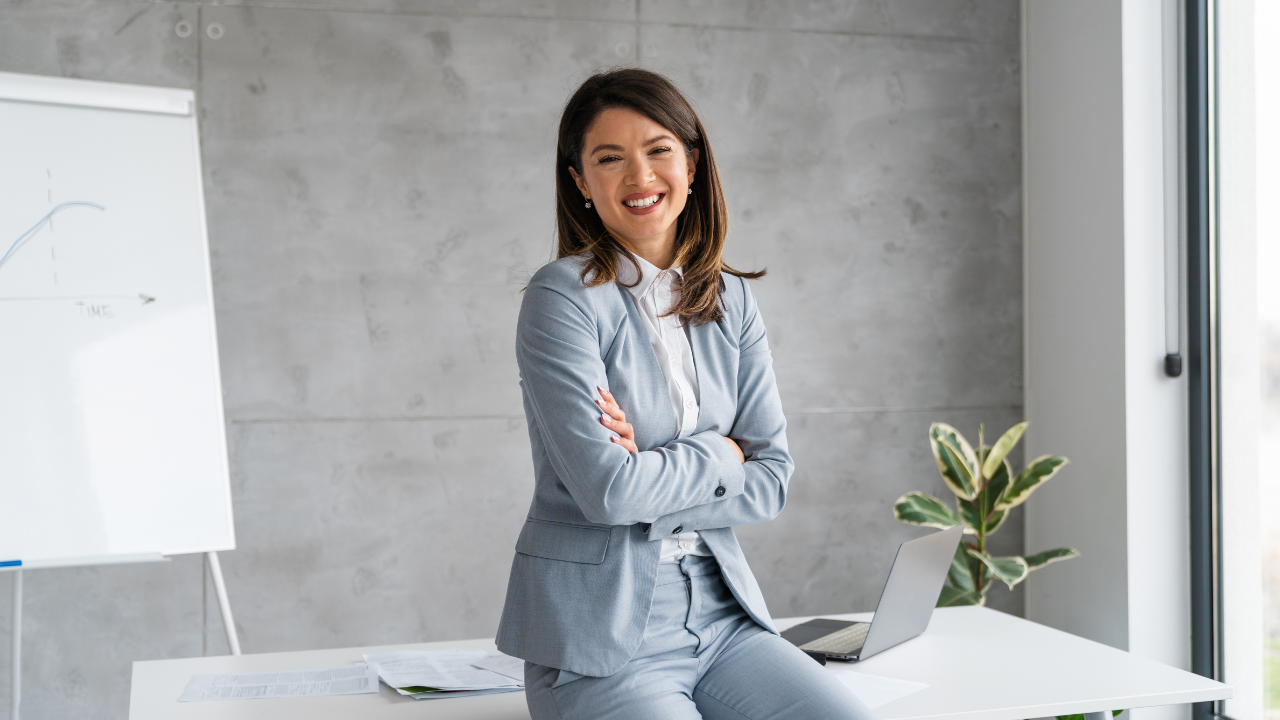 A business woman and entrepreneur sitting in her office smiling with her arms crossed | Scott Legal, P.C. A business woman and entrepreneur sitting in her office smiling with her arms crossed