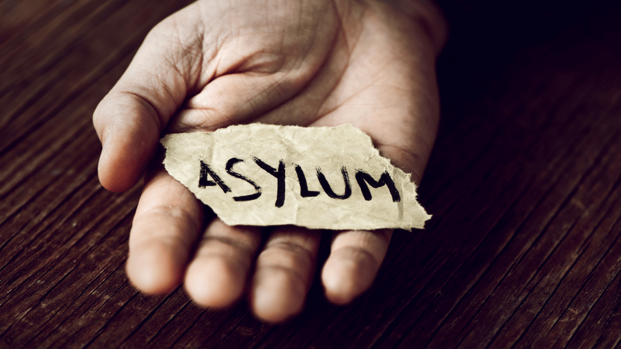 A hand holding a piece of paper that says "asylum" on it | Scott Legal, P.C. A hand holding a piece of paper that says "asylum" on it
