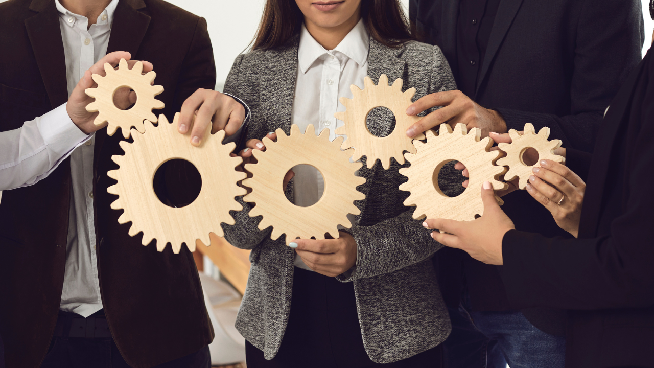 A group of business men and women holding gears in cooperation | Scott Legal, P.C. A group of business men and women holding gears in cooperation