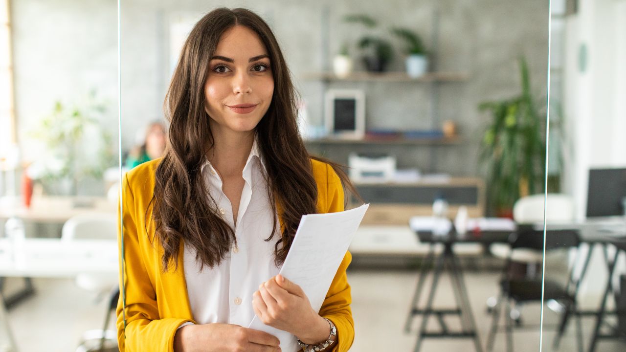 A business woman smiling at the camera while standing in an office, holding a folder | Scott Legal, P.C. A business woman smiling at the camera while standing in an office, holding a folder