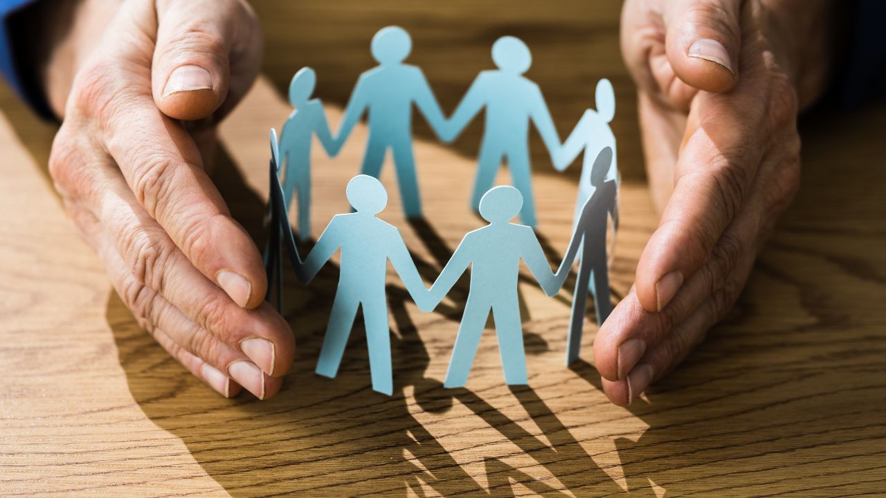 a hand protecting cut outs of people holding hands | Scott Legal, P.C. a hand protecting cut outs of people holding hands