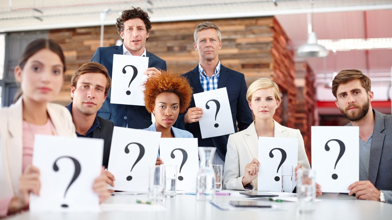A bunch of people holding question marks while in the office | Scott Legal, P.C. A bunch of people holding question marks while in the office