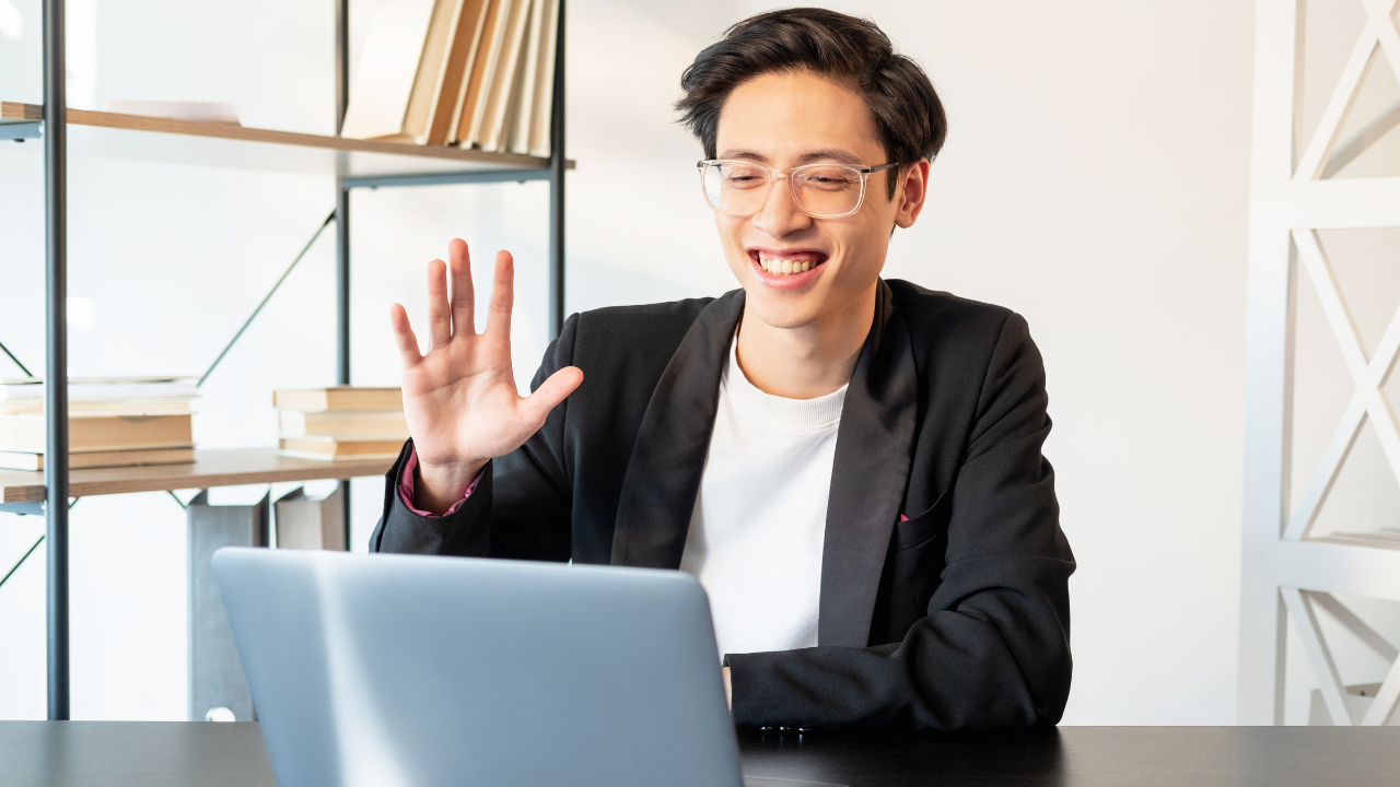 A man smiling at his laptop and waving | Scott Legal, P.C. A man smiling at his laptop and waving