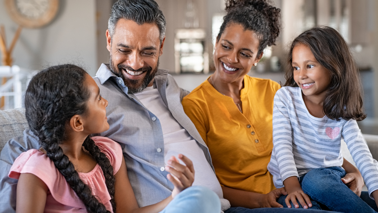 A happy family of 4 sitting on their couch | Scott Legal, P.C. A happy family of 4 sitting on their couch