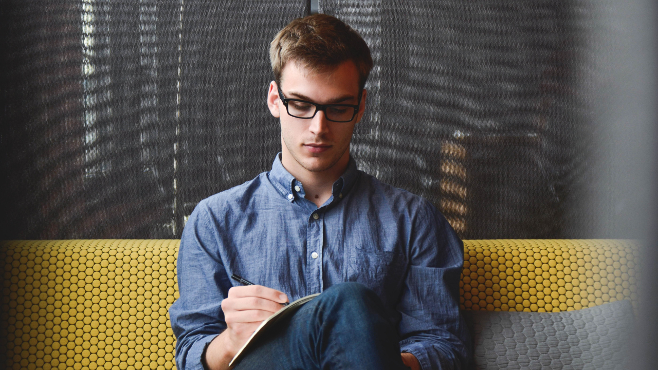 A man writing on pen and paper while sitting down | Scott Legal, P.C. A man writing on pen and paper while sitting down