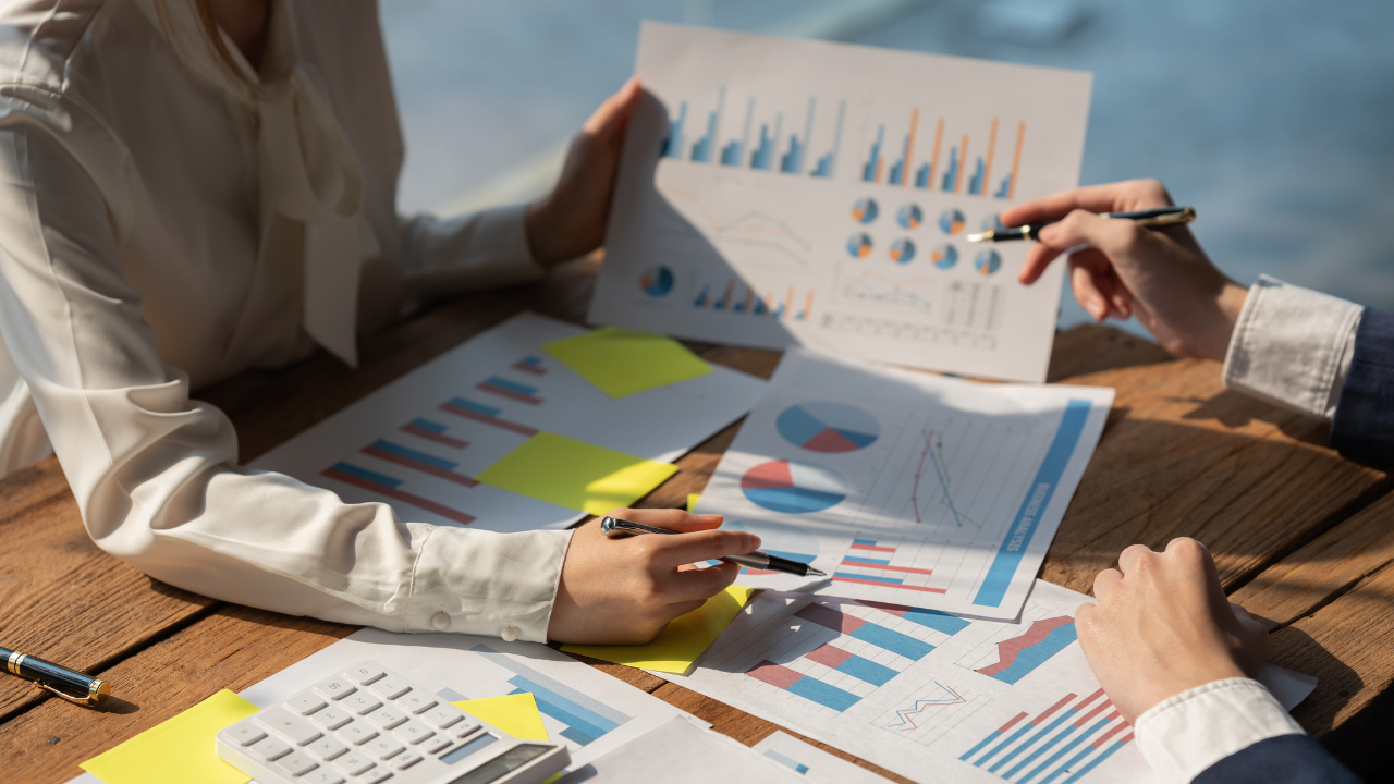 Two individuals looking at a bunch of graphs on the table. | Scott Legal, P.C. Two individuals looking at a bunch of graphs on the table.